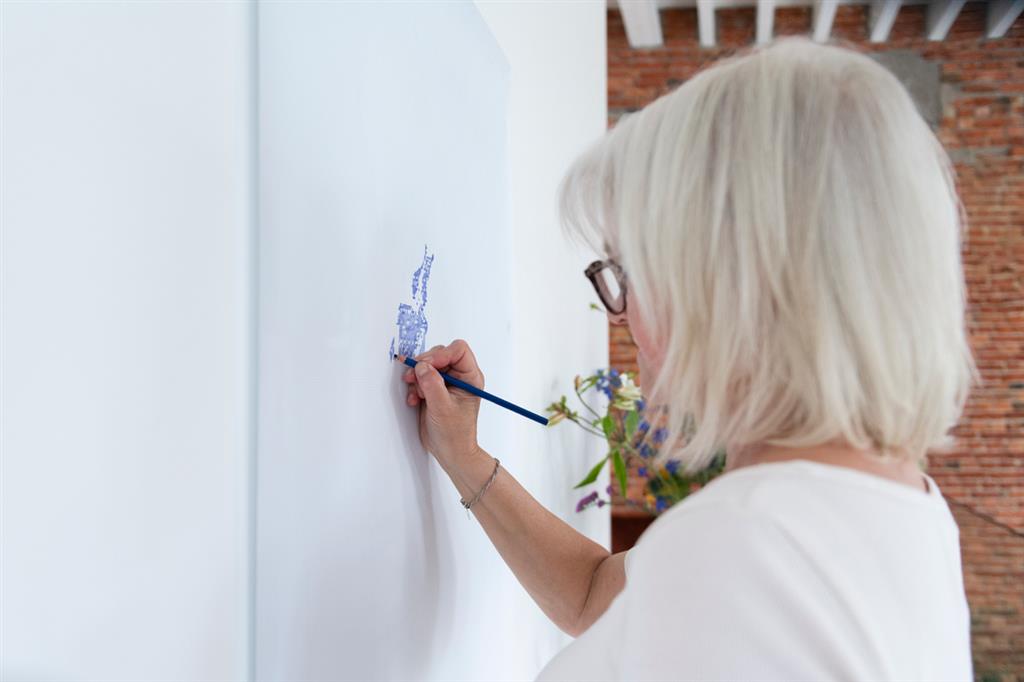 Personne dessinant sur un grand mur blanc avec un stylo, plongée dans sa création artistique.